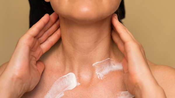 A woman applying cream to her neck.