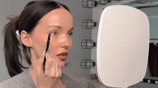 Dove Cameron holding a white mirror and applying makeup